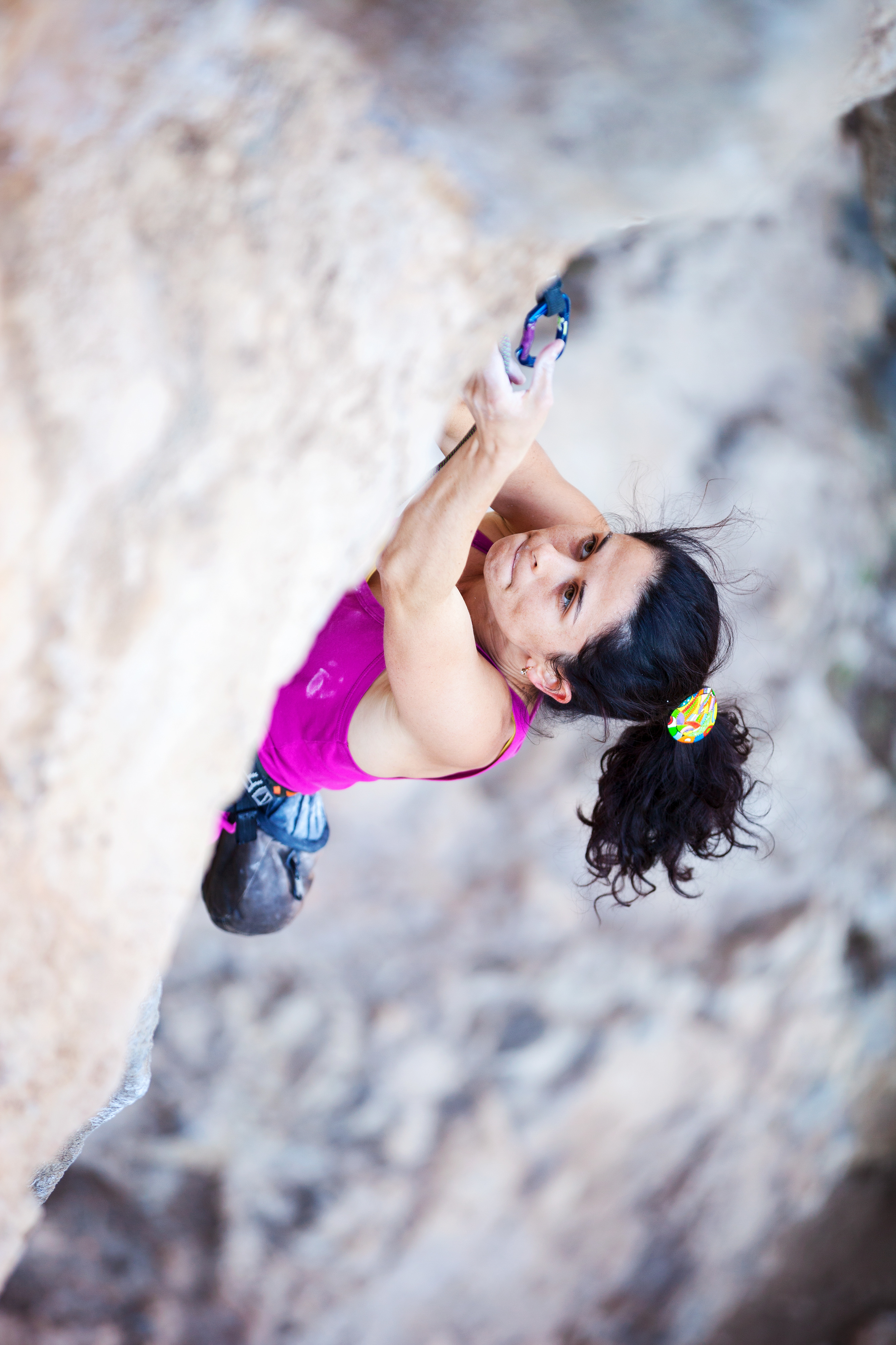 Young female rock climber clipping rope while lead climbing